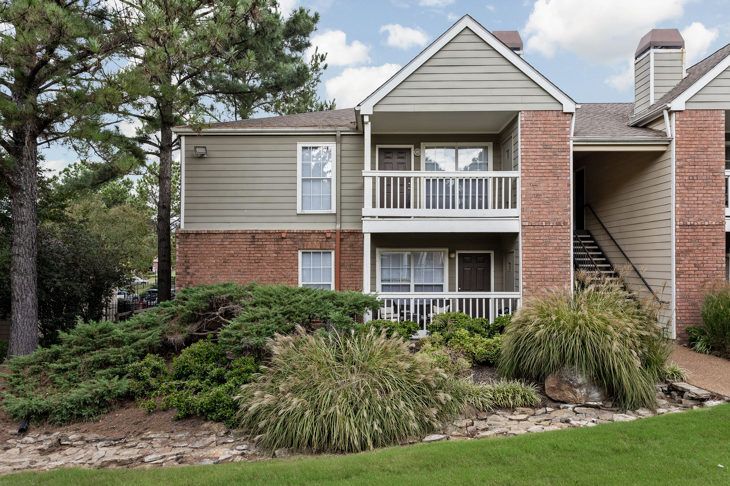 Exterior of brick apartment building with private patios and balconies surrounded by landscaping