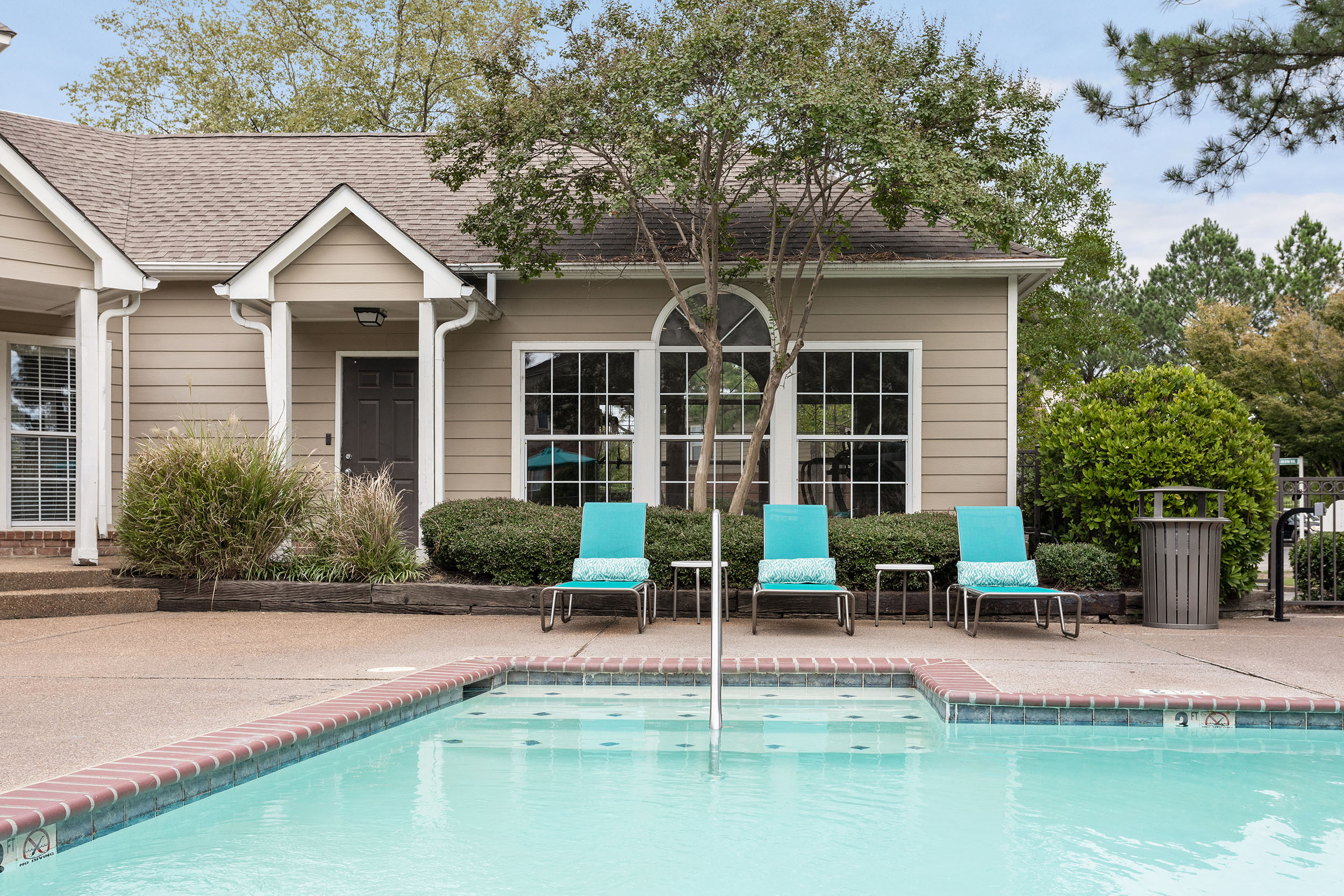 Railing and steps down in to pool in front of blue lounge chairs and apartment clubhouse