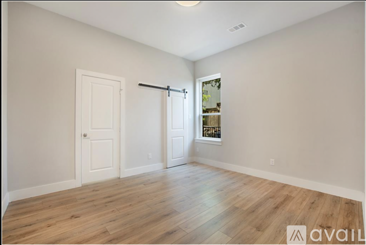 A room with wooden flooring and white walls, with a door and a window with a view of trees.