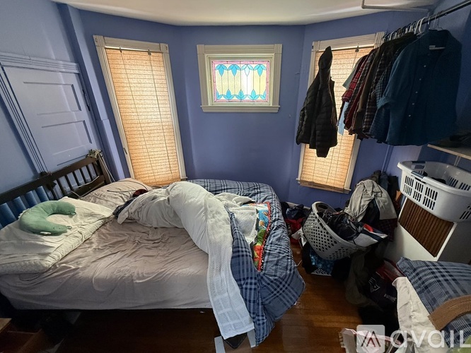 A messy bedroom with a bed, clothes, and a window with blinds.