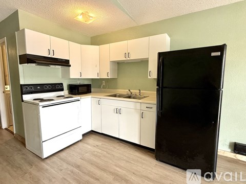 A kitchen with white cabinets and a black refrigerator.