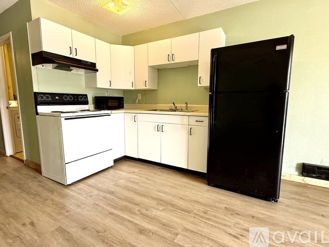 A kitchen with white appliances and cabinets, a black refrigerator, and a wooden floor.