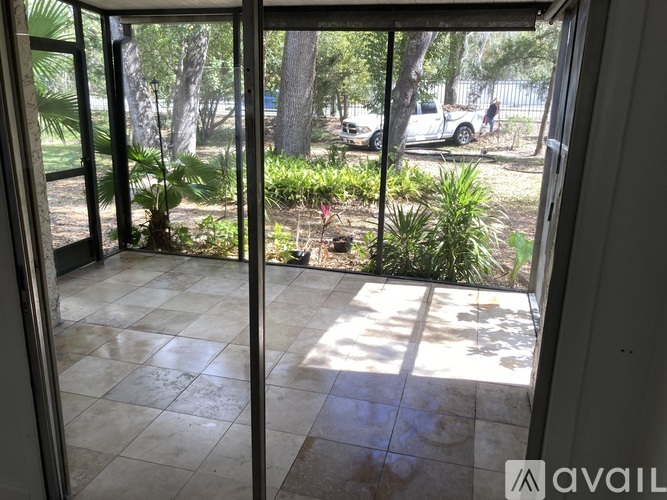 A view from inside a room looking out to a patio with a car and trees in the background.