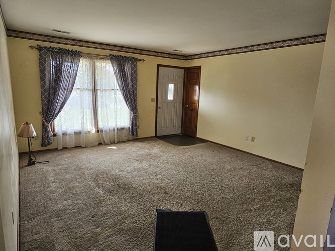 A room with a carpeted floor and a window with a curtain.