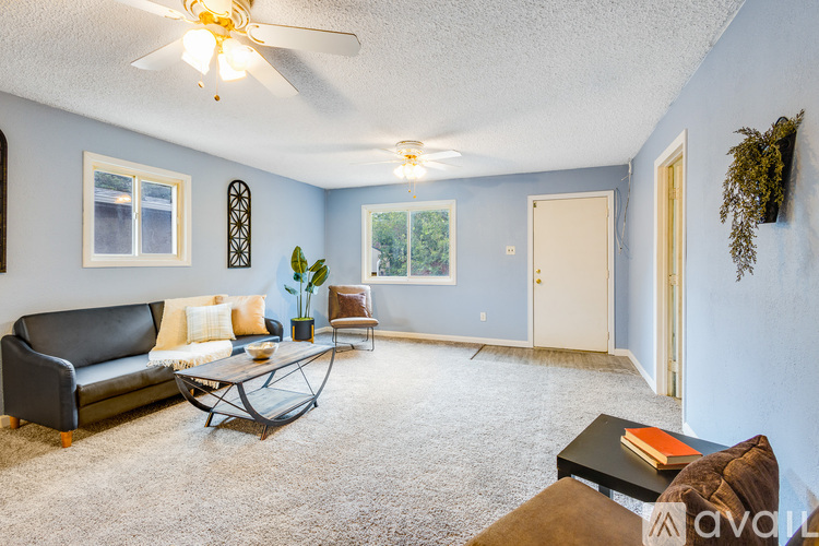A living room with a black leather couch, a glass coffee table, and a ceiling fan.