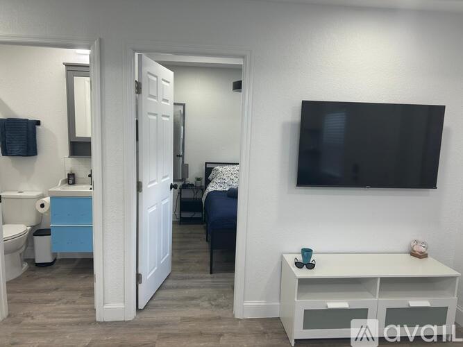 A small bedroom with a bed, a nightstand, a toilet, a sink, and a television.