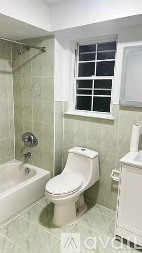 A white toilet is in a bathroom with green tiles.