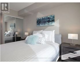 A bedroom with a large bed, a nightstand with a lamp, and a painting on the wall.
