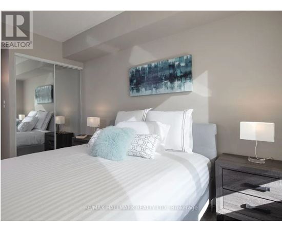 A bedroom with a large bed, a nightstand with a lamp, and a painting on the wall.