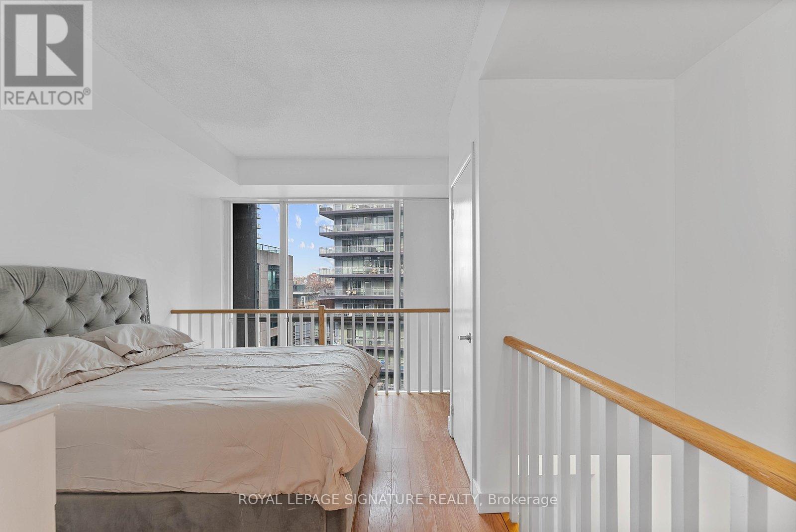 A bedroom with a large bed and a view of a balcony with buildings outside.