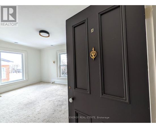A black door with a brass handle is in the foreground of a room with a carpeted floor and a window.