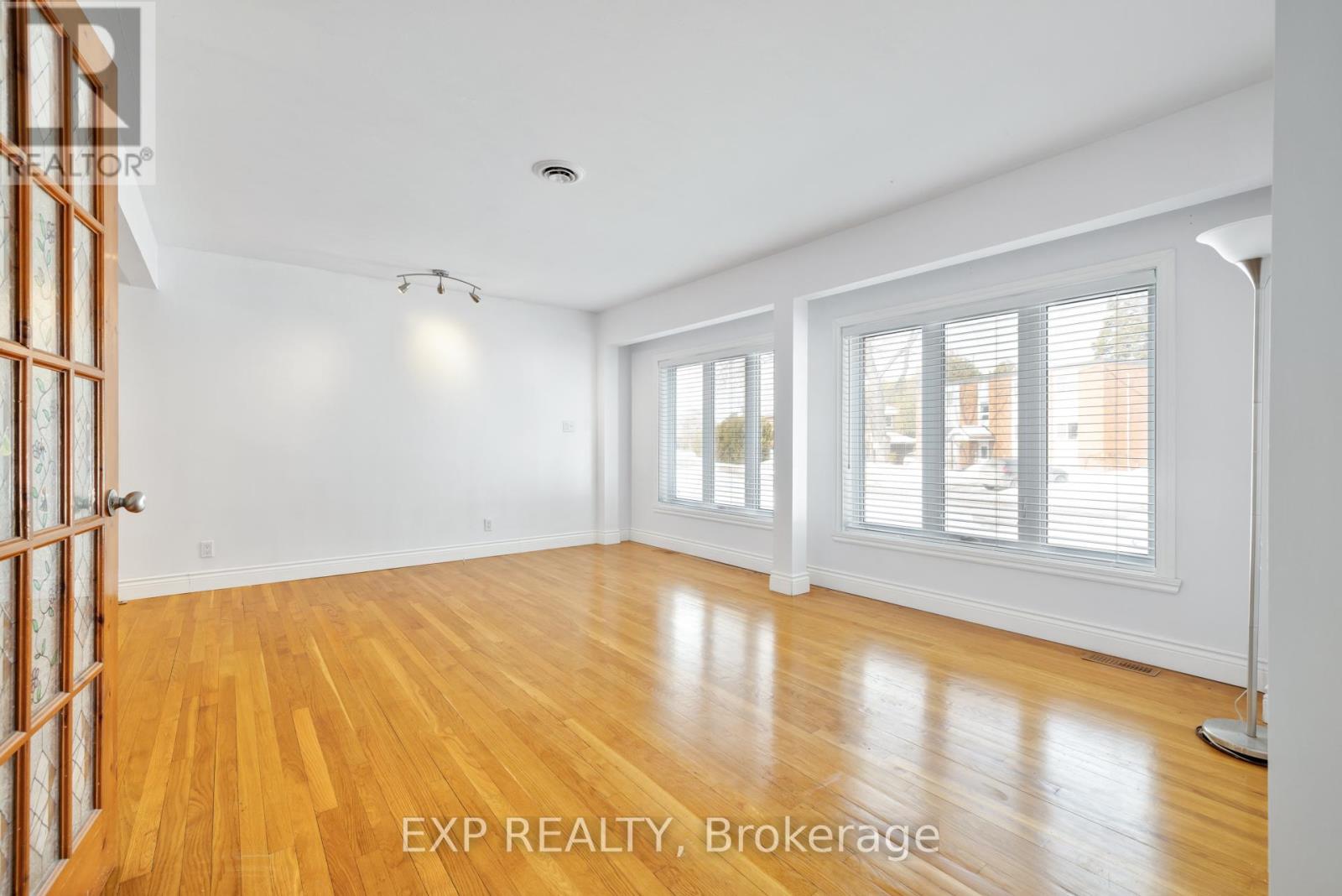 A room with wooden floors and white walls, with a door on the left and a window on the right.