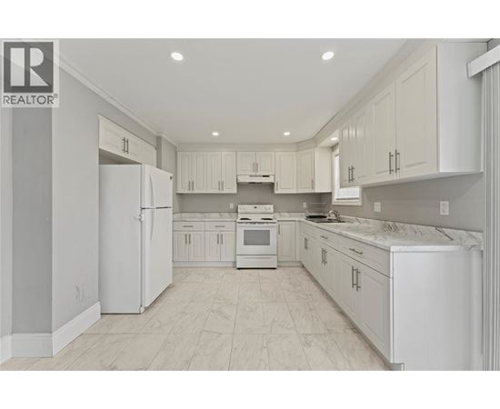 A white kitchen with a refrigerator, sink, and cabinets.