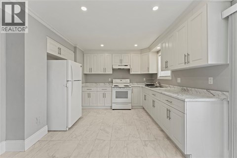 A white kitchen with a refrigerator, sink, and cabinets.