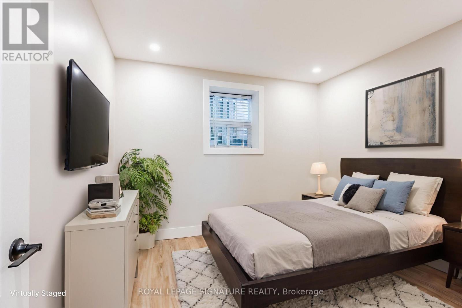 A bedroom with a bed, nightstand, and a plant.