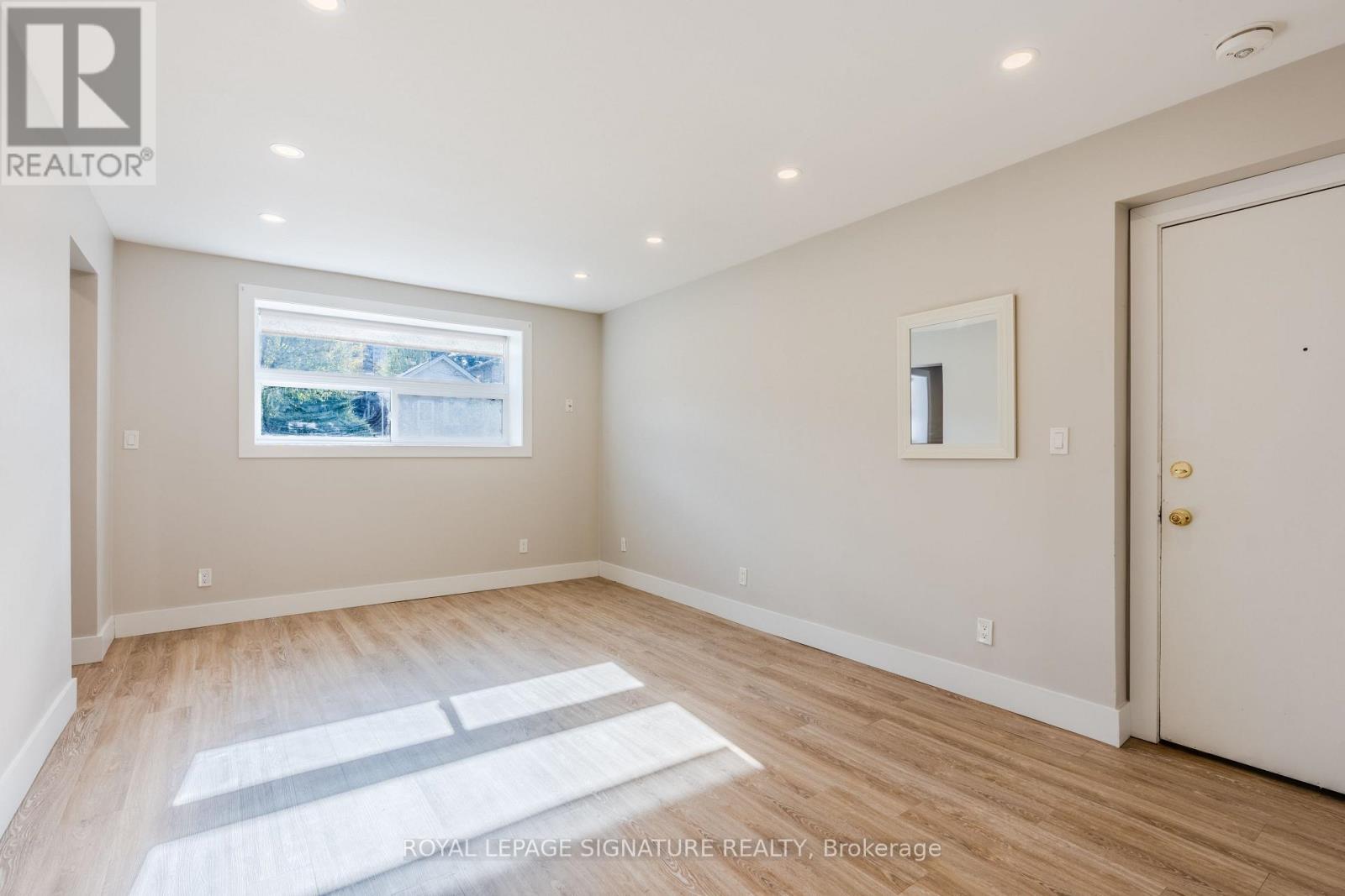 A spacious room with a window, wooden flooring, and a white door.