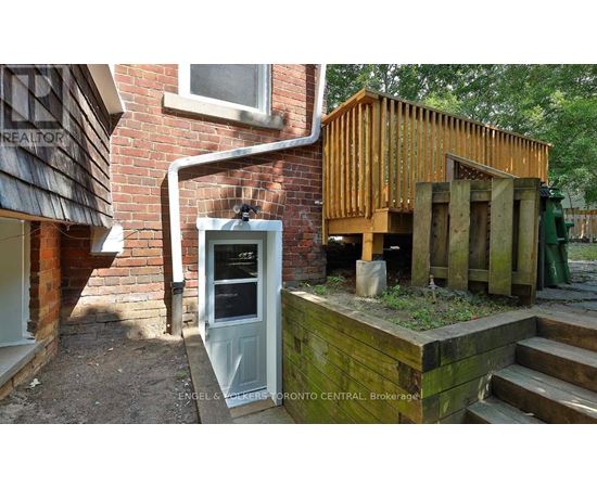 A wooden structure with a door is in front of a brick building.