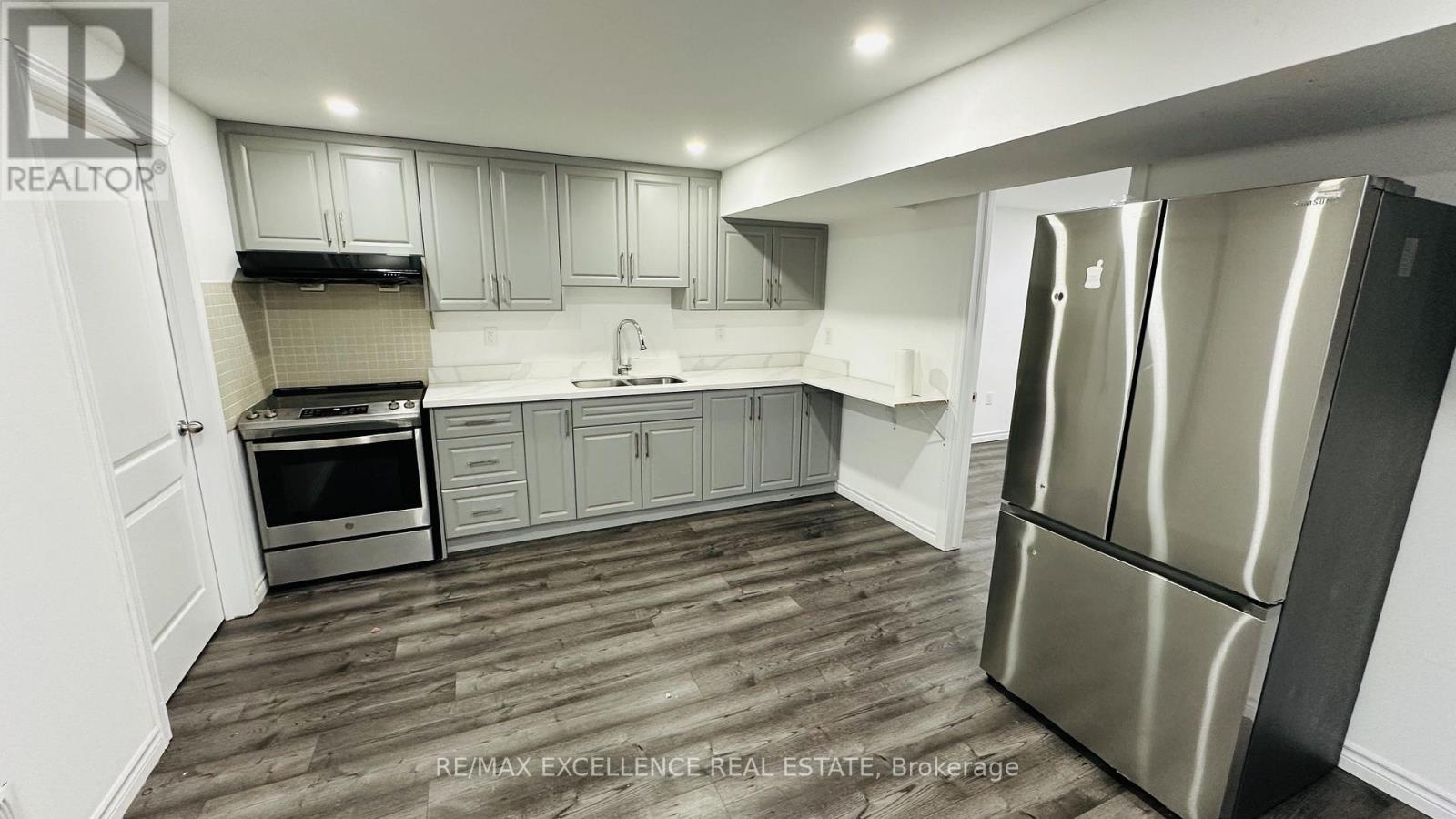 A modern kitchen with a stainless steel refrigerator and wooden flooring.
