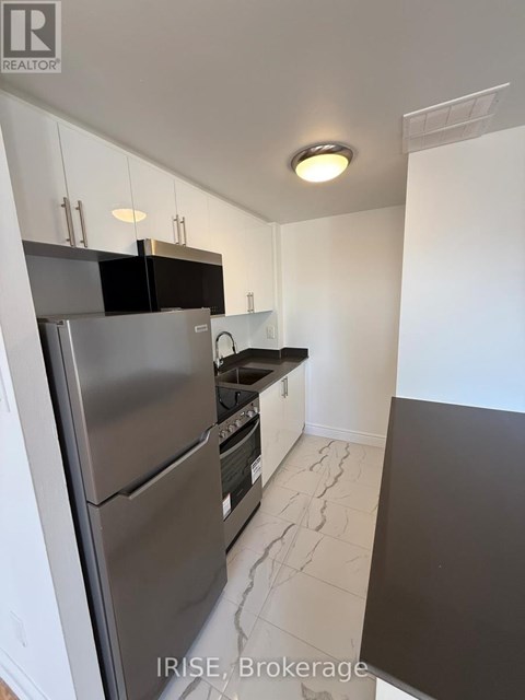 A kitchen with a stainless steel refrigerator and black countertops.