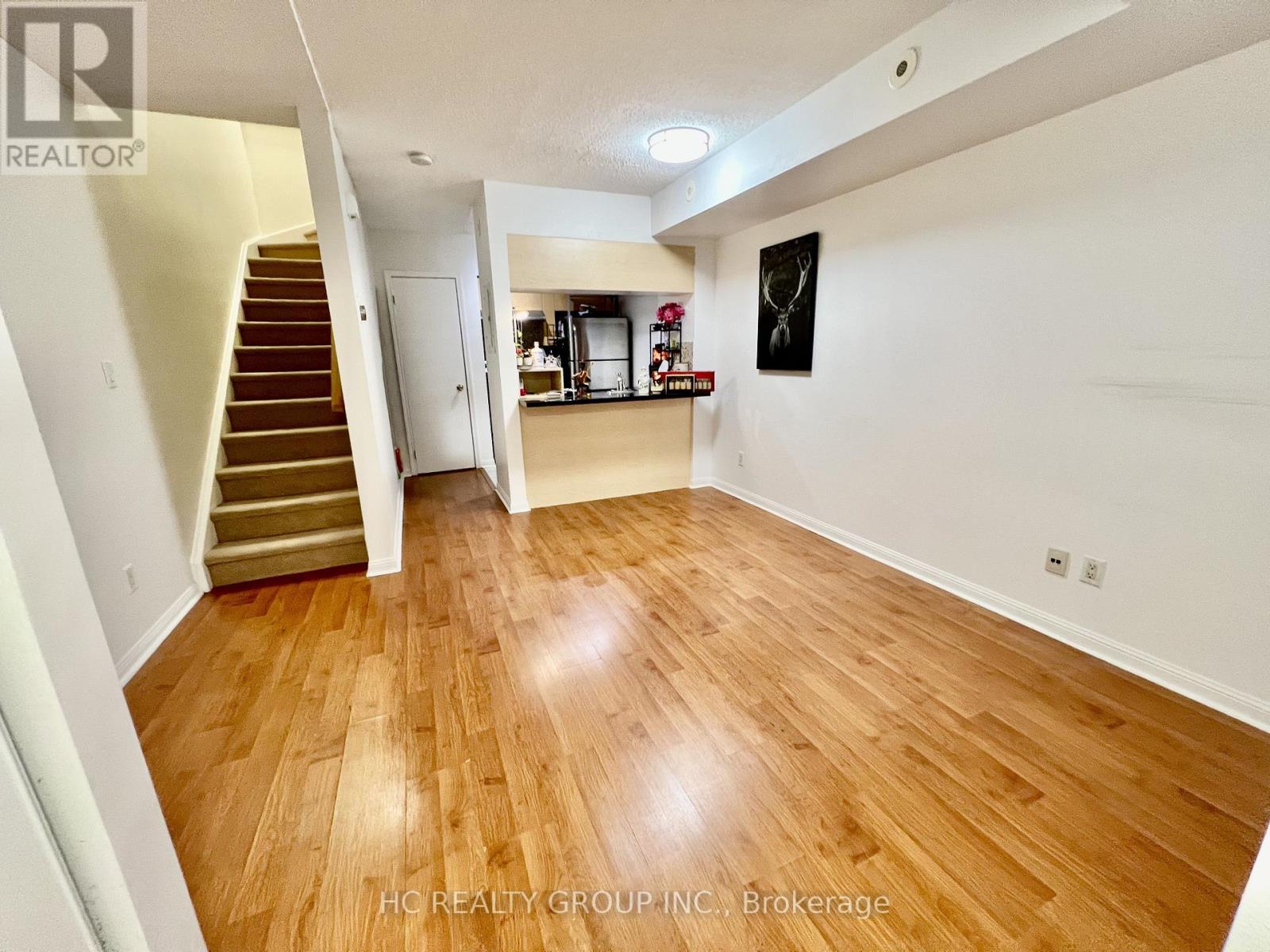 A room with wooden flooring and a staircase leading to another room.