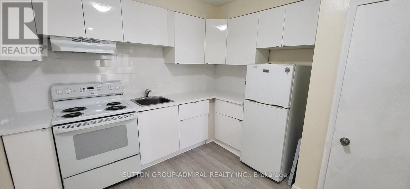 A white kitchen with a stove, sink, and refrigerator.