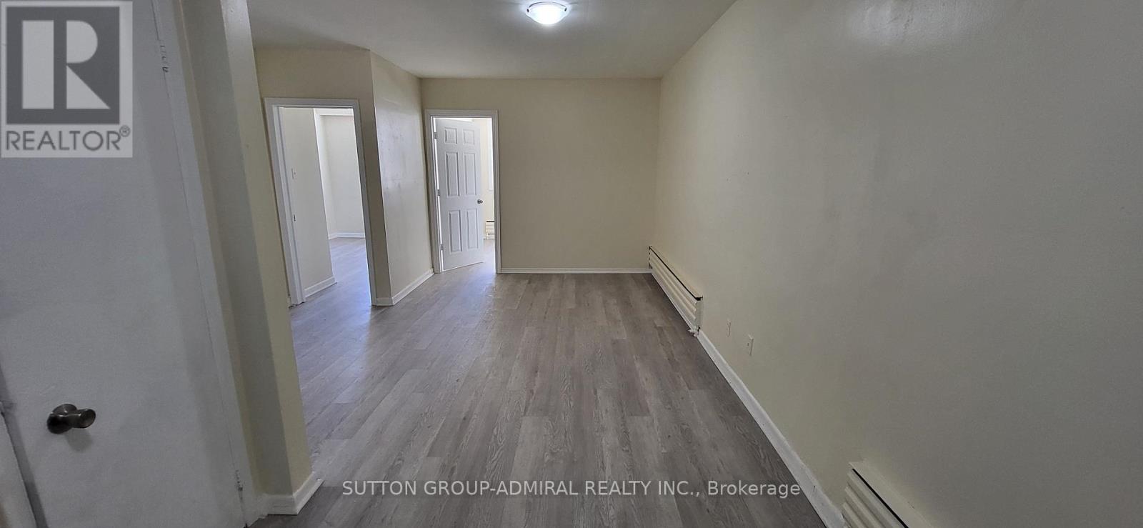 A brokerage sign is on the door of a room with wood flooring and white walls.