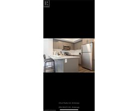 A kitchen with a refrigerator, microwave, and a bar stool.