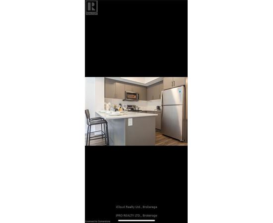 A kitchen with a refrigerator, microwave, and a bar stool.