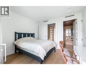 A bedroom with a bed, chair, and a wooden floor.