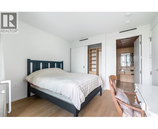 A bedroom with a bed, chair, and a wooden floor.