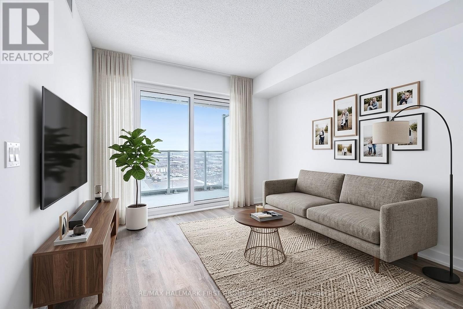 A living room with a grey couch, a coffee table, a flat screen TV, and a large window with a view of the city.