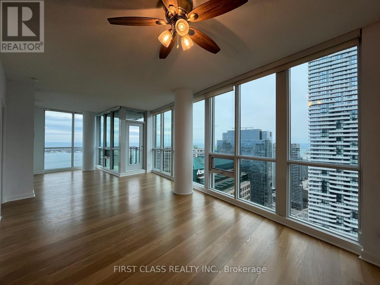 A spacious room with a ceiling fan and large windows overlooking a cityscape.
