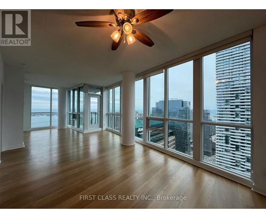A spacious room with a ceiling fan and large windows overlooking a cityscape.