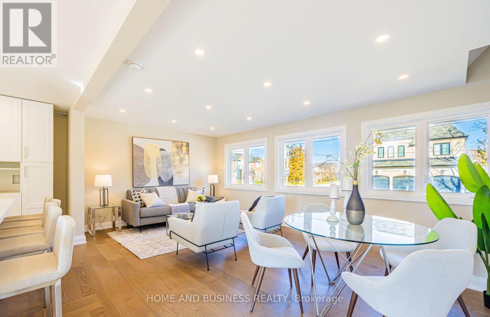 A well-lit, modern living room with a glass table and white chairs.