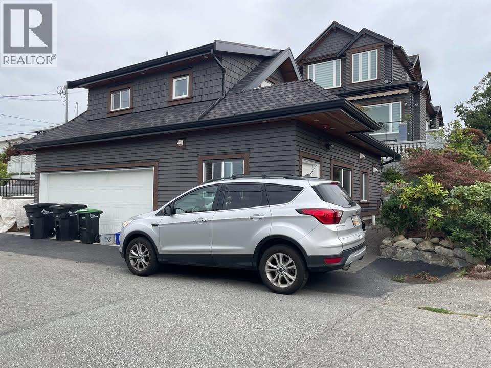 A silver car is parked in front of a grey house.