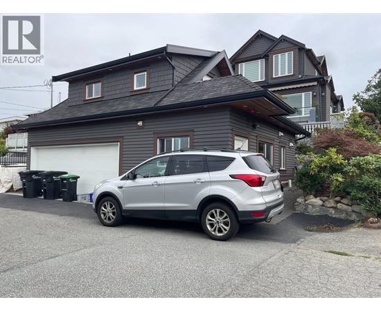 A silver car is parked in front of a grey house.