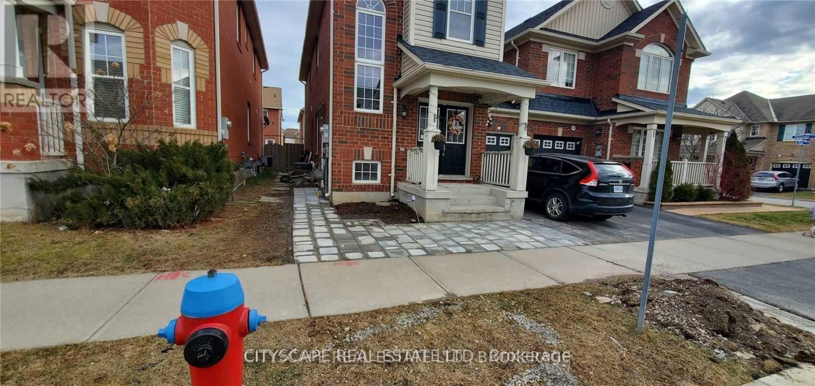 A red fire hydrant is in front of a brick house.