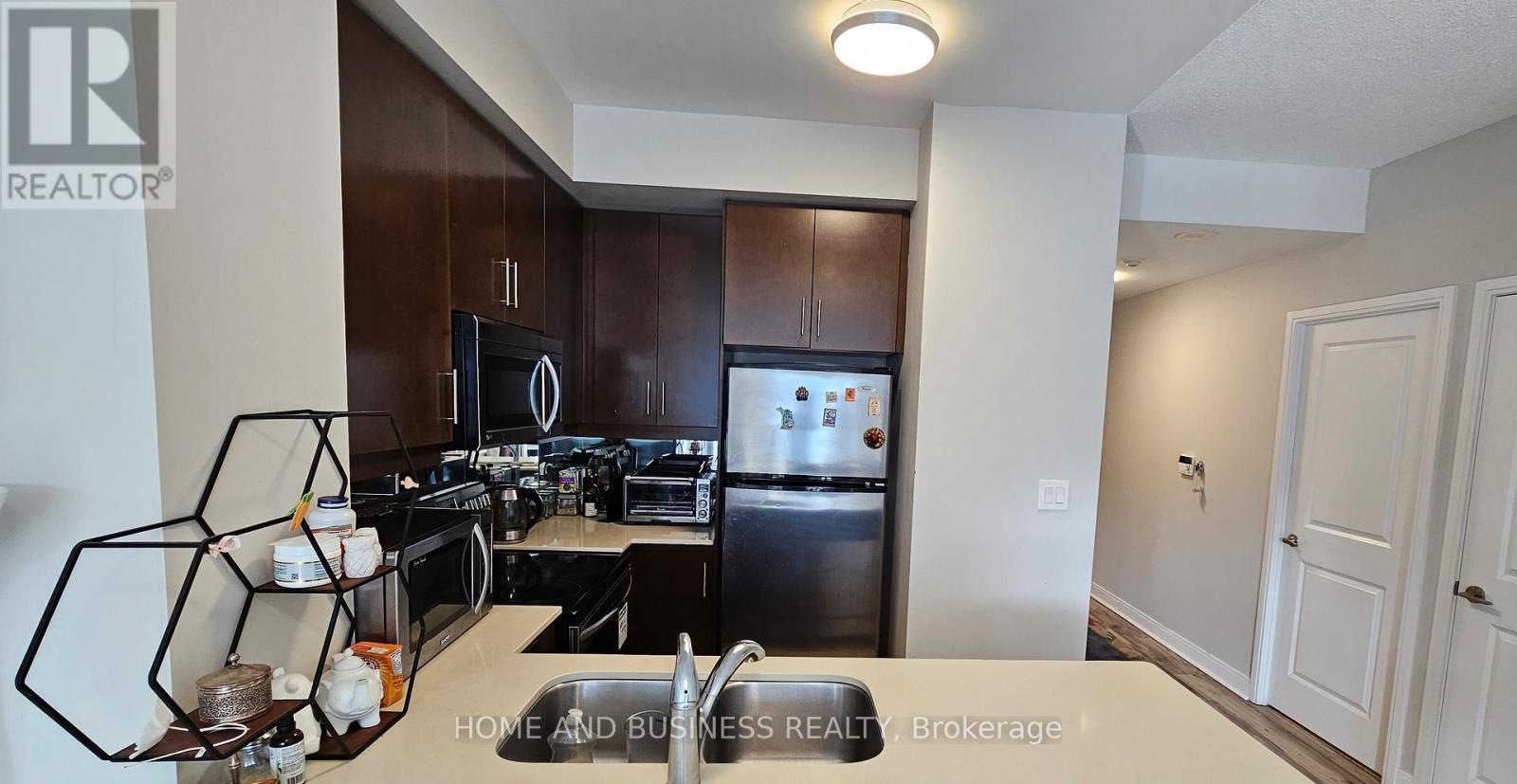 A well-lit kitchen with dark brown cabinets and a stainless steel refrigerator.