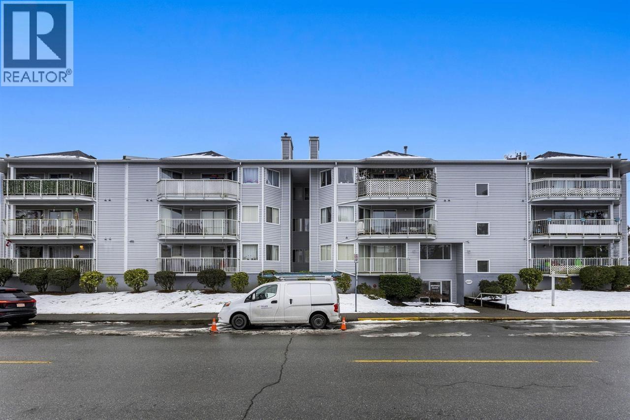A white van is parked in a parking lot in front of a large apartment building.