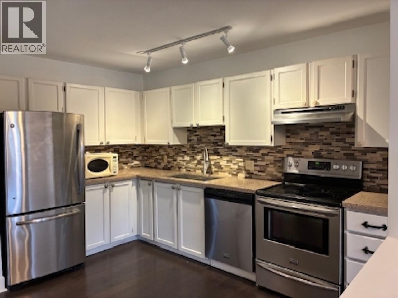 A kitchen with a refrigerator, oven, microwave, and sink.