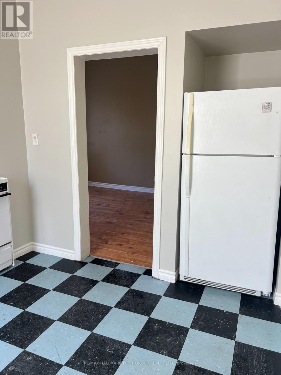 A black and white checkered floor in a room with a white fridge and a doorway.