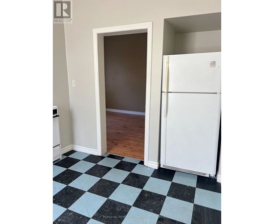 A black and white checkered floor in a room with a white fridge and a doorway.