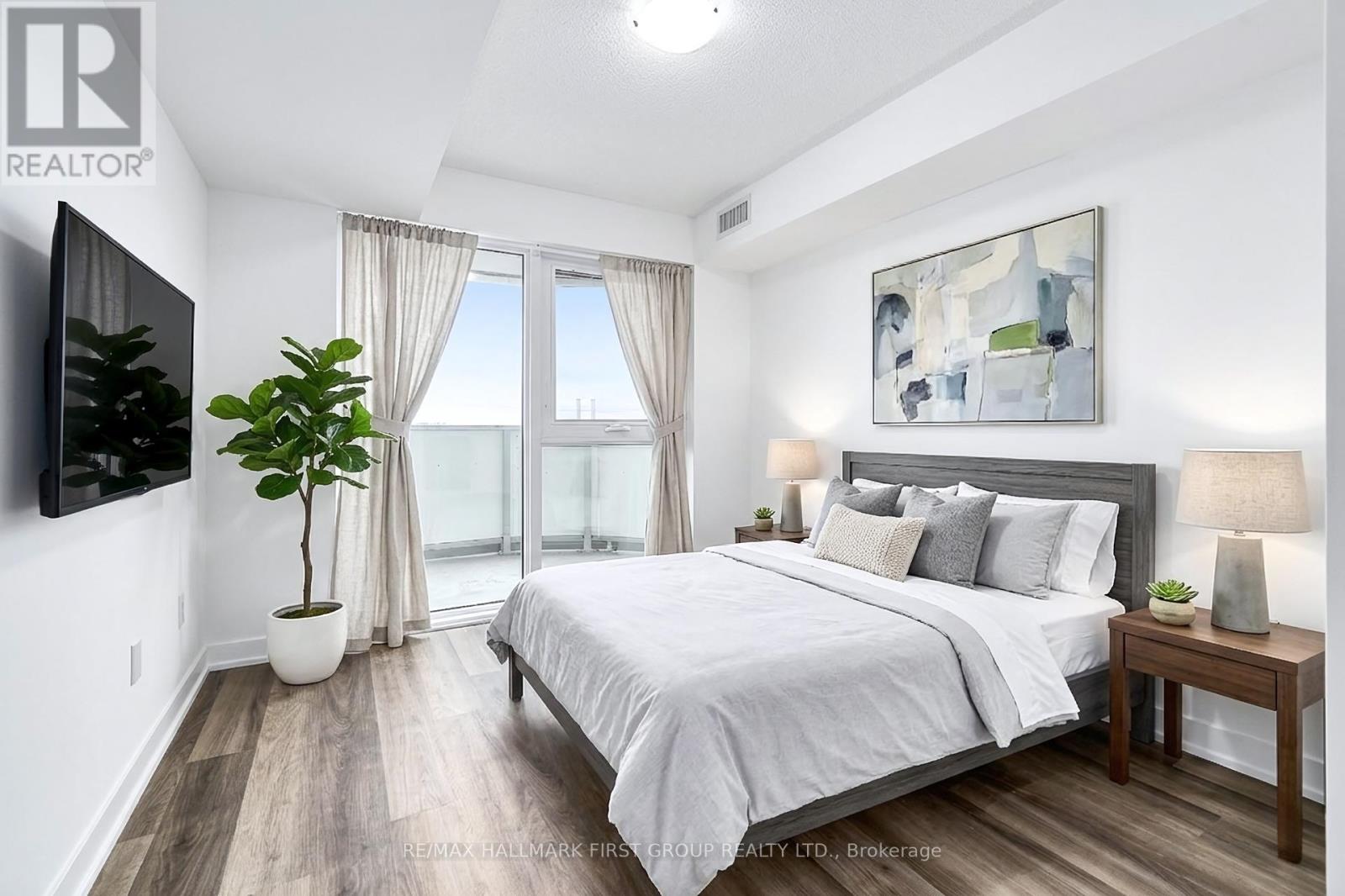 A bedroom with a large bed, a flat-screen TV, and a view of the ocean through the window.