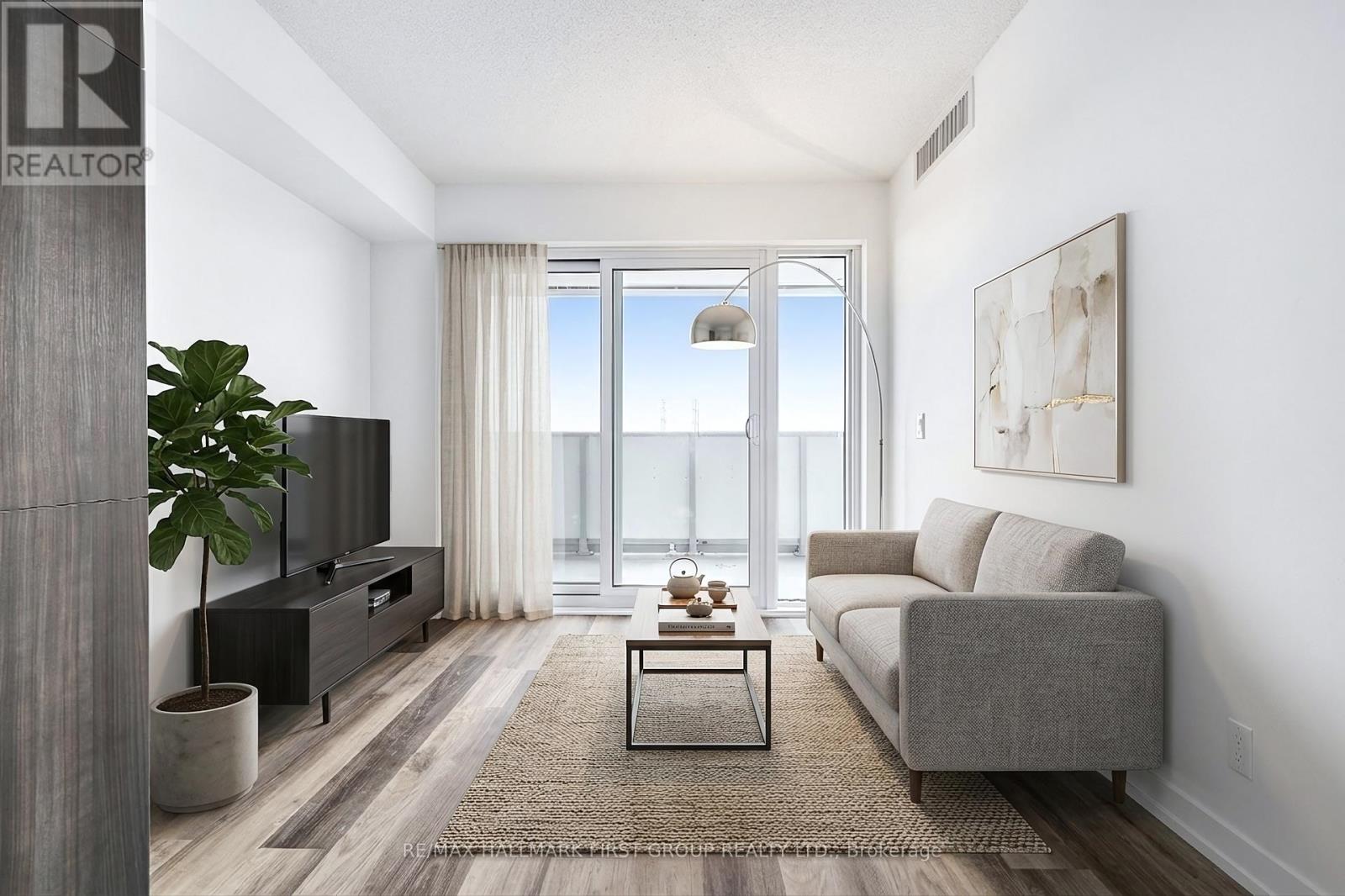 A living room with a grey couch, a wooden cabinet, a coffee table, and a large window with a view of the city.