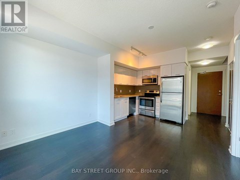 A kitchen with white cabinets and stainless steel appliances in a white room with a dark floor.