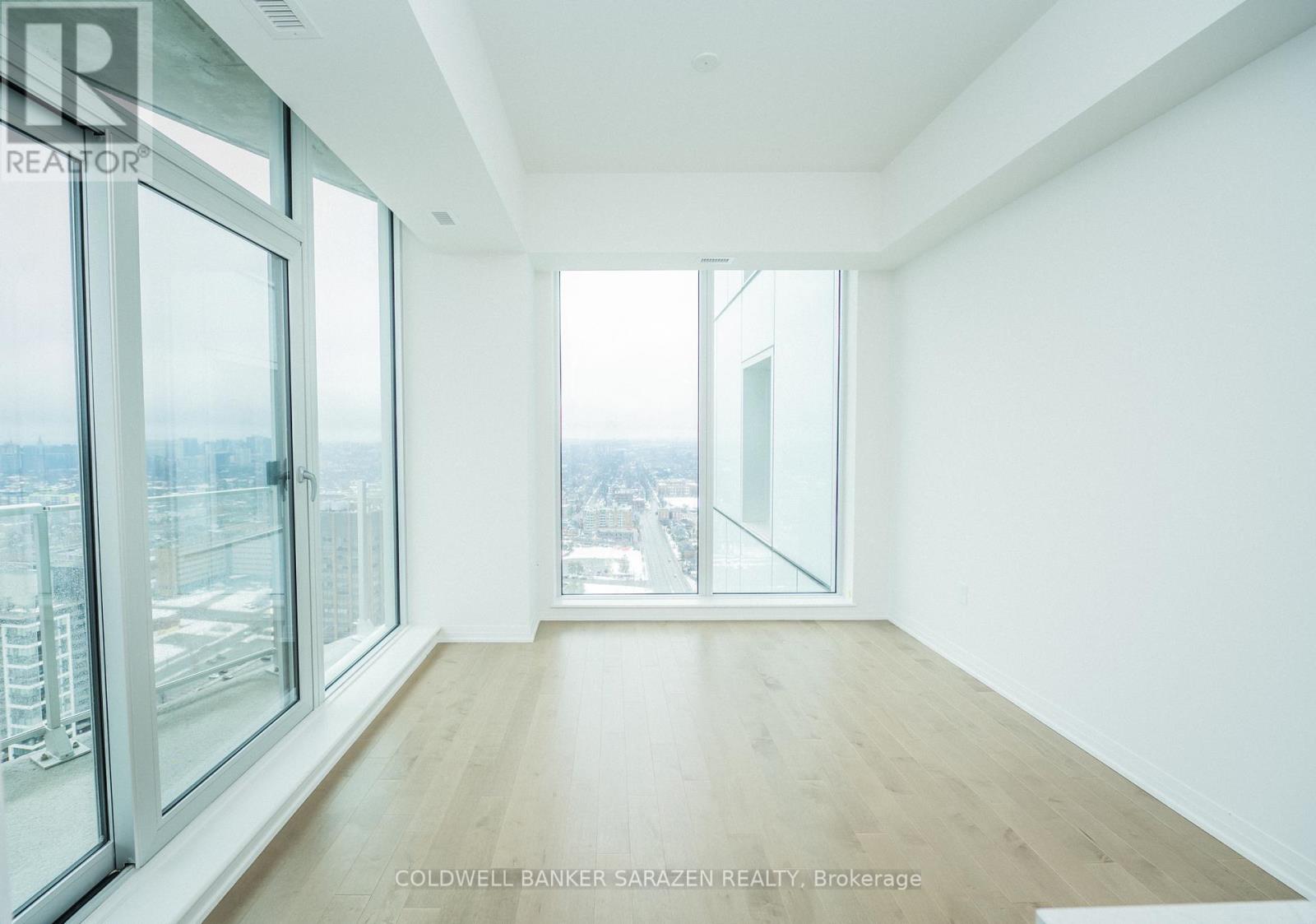 A spacious room with wooden floors and large windows overlooking a cityscape.