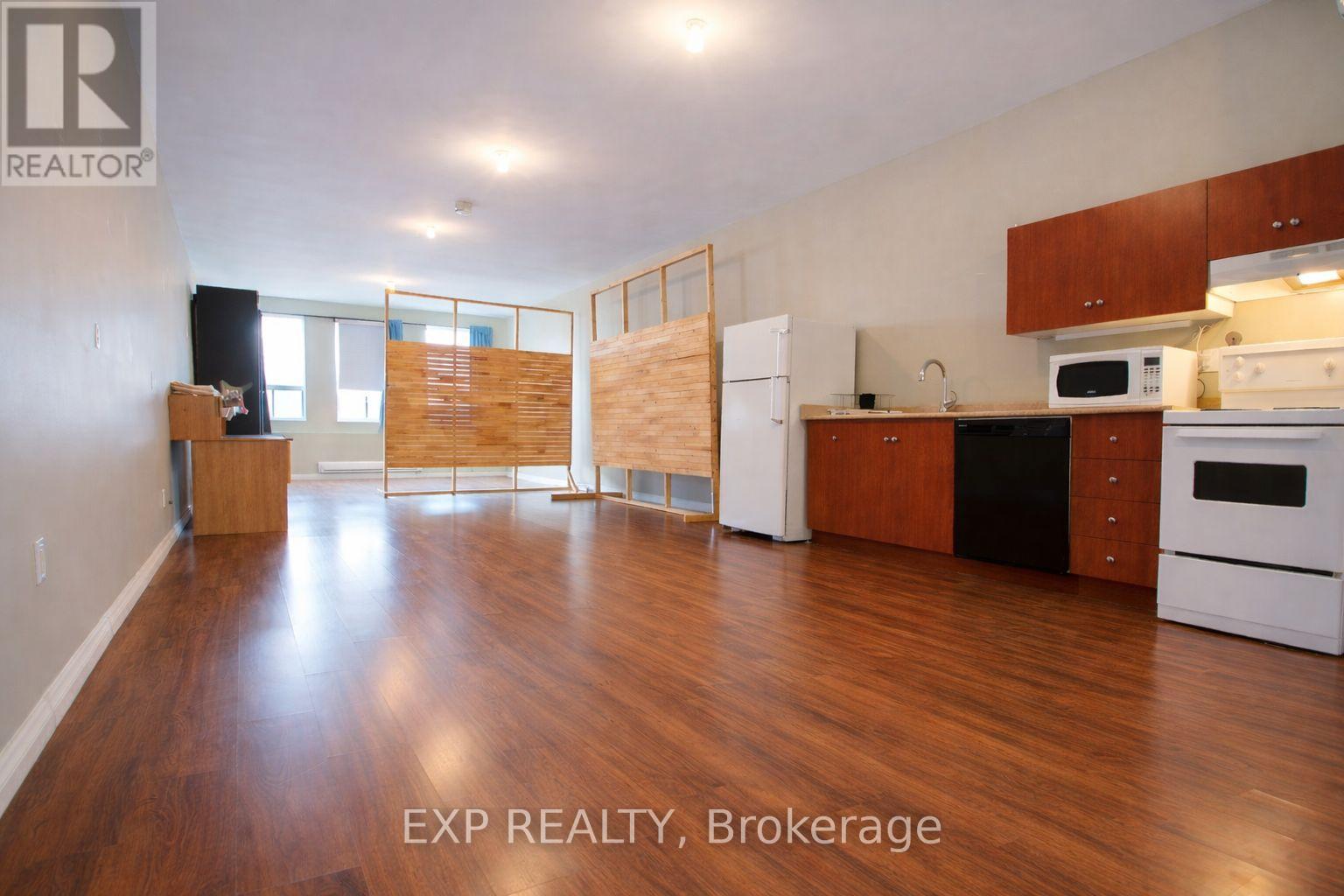 A large open room with wood floors and a kitchen area with white appliances.