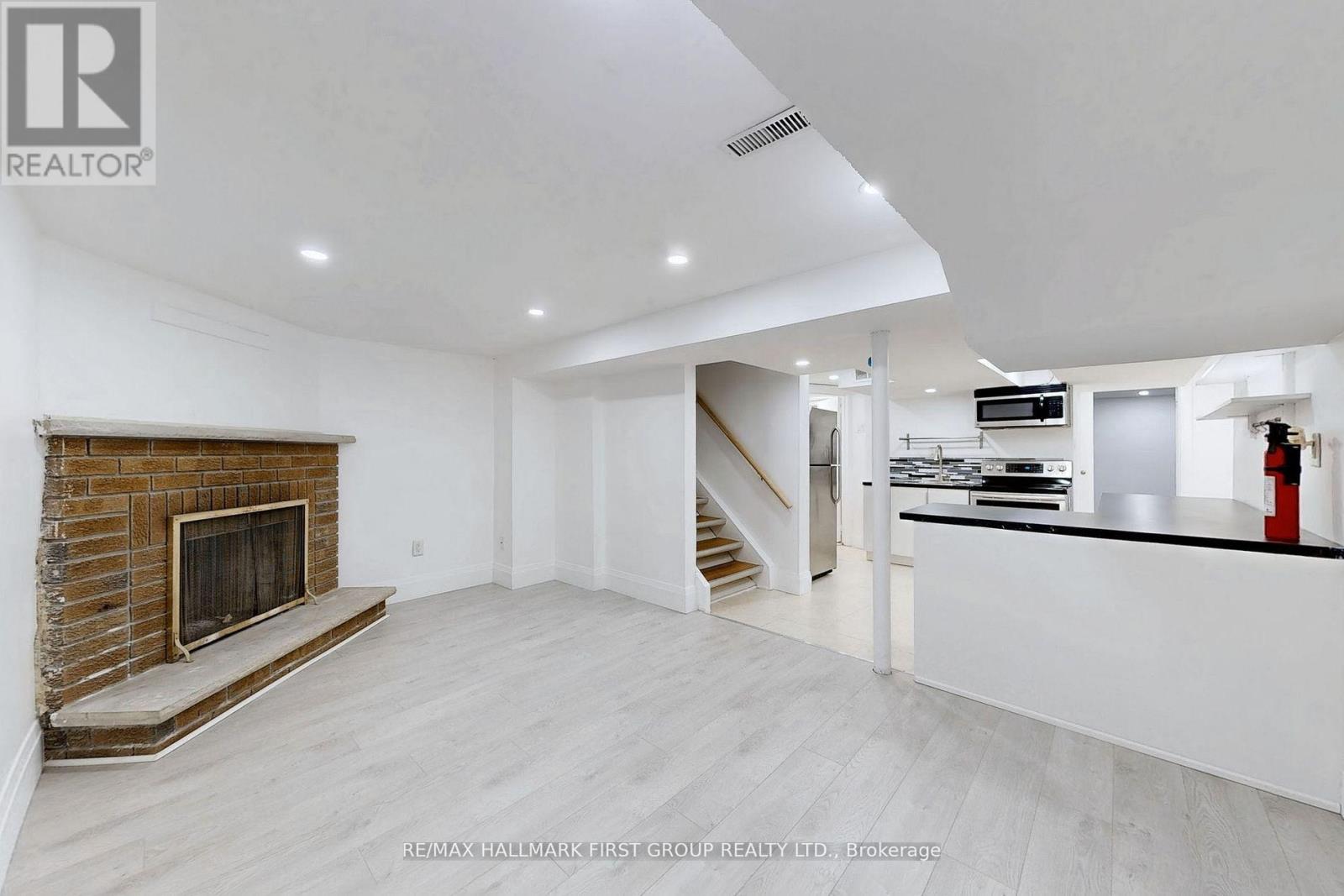 A spacious living room with a fireplace and a staircase leading to the kitchen.
