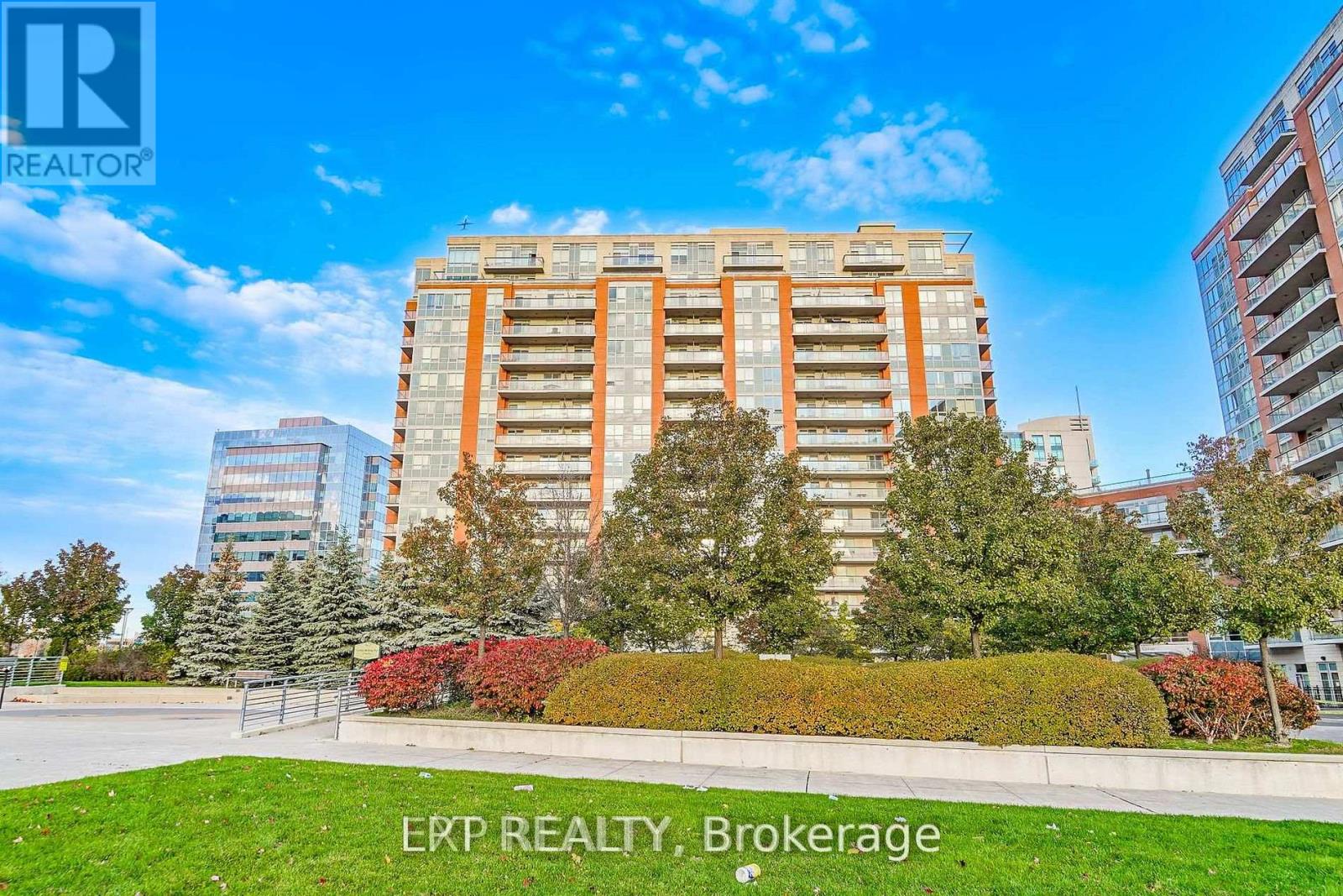 A tall apartment building with a green lawn in front and trees around it.