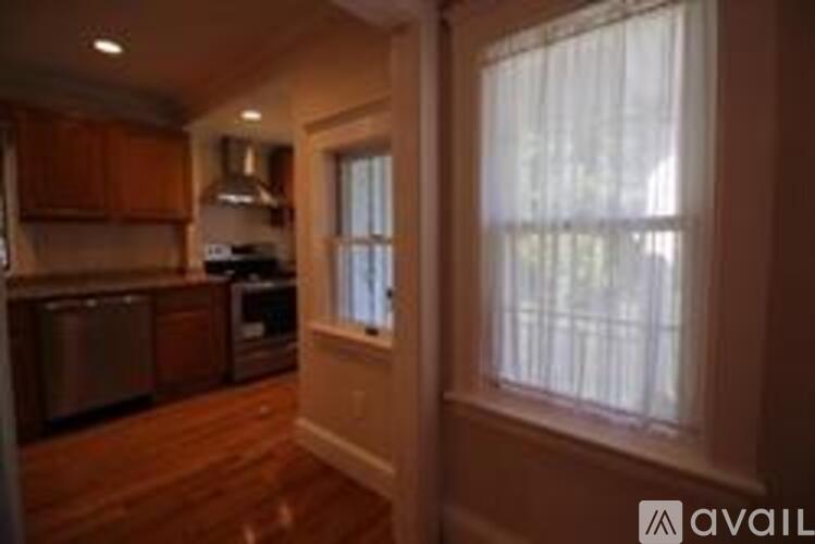 A kitchen with wooden cabinets and a window with white curtains.